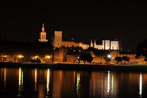 Papal Palace in the city of Avignon, France illuminated at night with the river Rhine embankment.