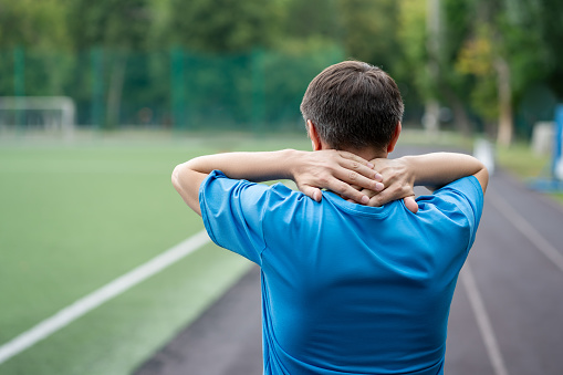 Neck pain, athletic man with backache on a running track after workout, health problems concept