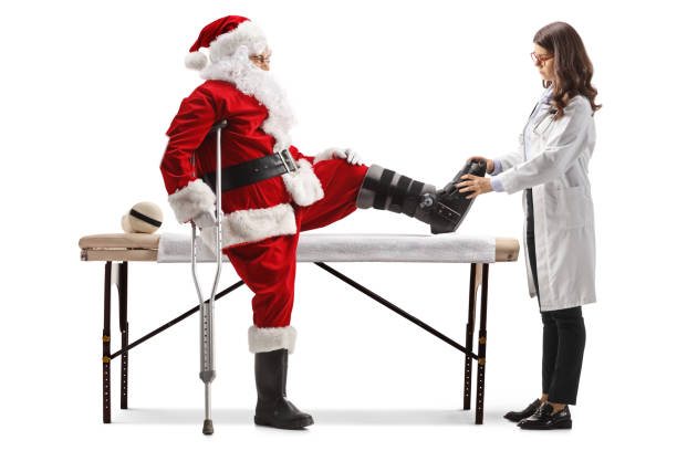 médecin vérifiant le père noël avec une attelle de pied et une béquille - christmas crutch holiday christmas decoration photos et images de collection