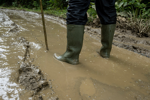 A dirty military boot covered in mud stands in a puddle. The worn footwear suggests hard use and a rugged environment. The muddy water adds a sense of grit and grime to the scene