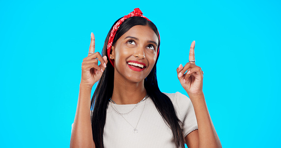 Face, motivation and Indian woman with decision, pointing and wellness against a blue studio background. Portrait, female and lady with smile, direction and choice with inspiration, promotion and joy