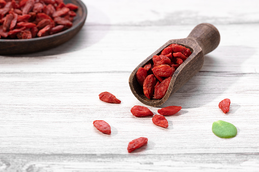 Dried goji berries on wooden spoon and wooden plate on white background.