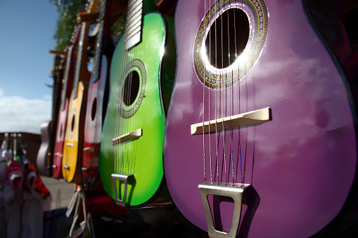 A stunning array of colorful, handcrafted guitars showcased in an outdoor marketplace. Each instrument reflects the sunlight, revealing its vibrant design and intricate patterns.