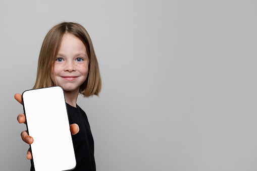 Joyful child holding smartphone with blank empty white screen display on gray background