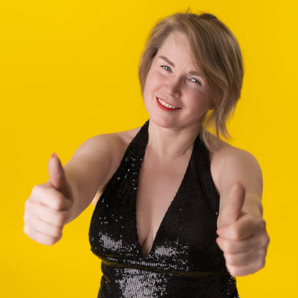 Portrait of curvy mature blonde in evening gown, giving two thumbs up and smiling with satisfaction stock photo