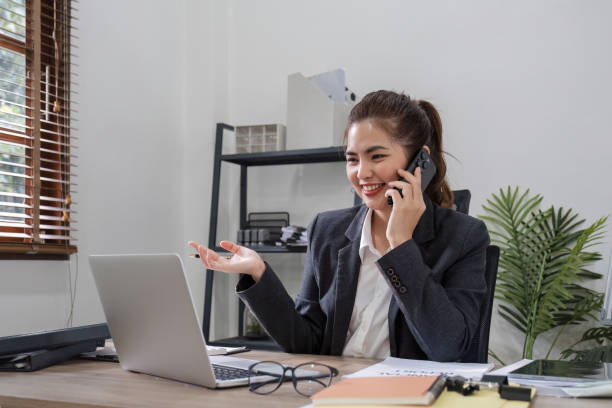 Asian female office worker with bright smile meeting via smartphone with business team, planning work and corporate marketing. Asian female office worker with bright smile meeting via smartphone with business team, planning work and corporate marketing.. smart phone telephone research tax stock pictures, royalty-free photos & images