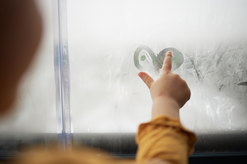 Beautiful girl drawing with finger on blurred window. Winter time.