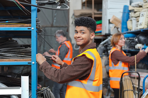 Young adult man recycling worker wearing orange reflective vests standing in warehouse and smiling at camera.