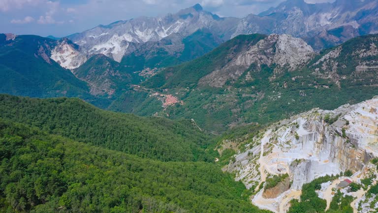 Aerial panning shot of marble quarry in Apuan Alps, Carrara, Italy. Sunny day, famous Carrara marble open-pit quarry in mountains.