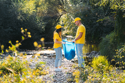 Male and female volunteers cleaning up garbage on the riverbank.