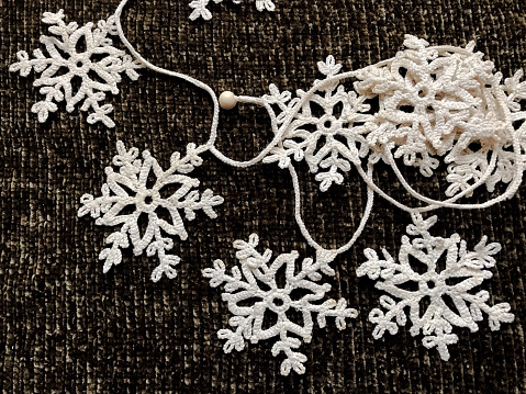 A pile of knitted white snowflakes in the form of a garland on a dark background. Snowflakes as a symbol of winter holidays create the right atmosphere and festive warm mood.