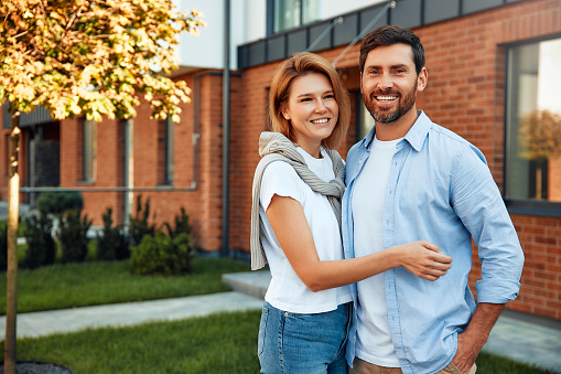 A young happiness married couple standing near a new house and hugging. Renting and buying a home. Moving concept.