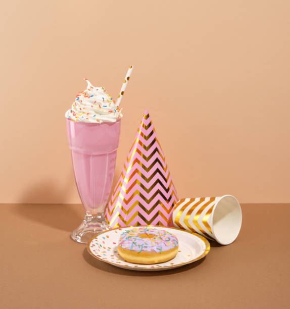Decorative and stylish birthday celebration. A delightful doughnut with colored glaze and sprinkles, a creamy milkshake and a festive hat.