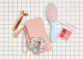 Women's pink wallet for money or business cards, eye shadow for fashionable and stylish makeup, hair comb, roller facial massager. Top view of make up acessories.