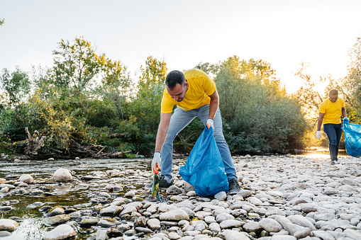 Young male volunteer cleaning up garbage on the riverbank.