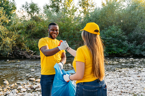 Male and female volunteer shaking hands in celebration after cleaning up garbage on the riverbank.
