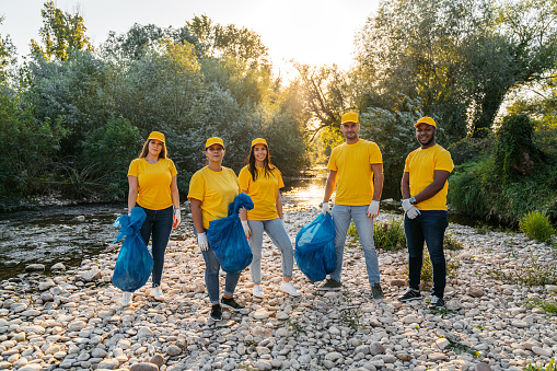 Portrait of a group of young nature conservation volunteers cleaning up garbage on the riverbank.