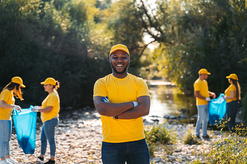 Portrait of a young black male nature conservation volunteer cleaning up garbage on the riverbank.