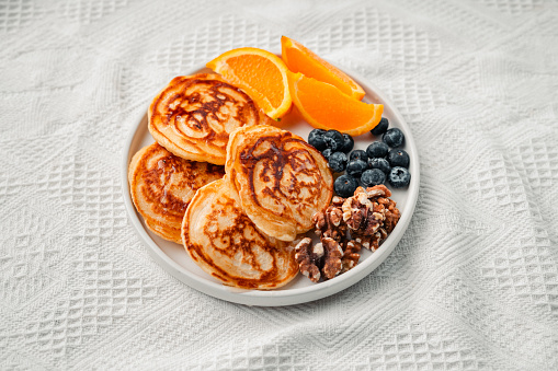 Pancakes, oranges, blueberries and walnuts in a white plate