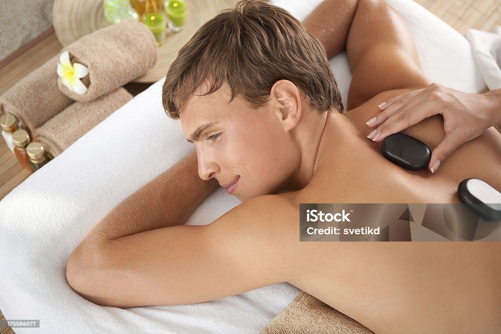 Men beauty and relax time. Young handsome man in SPA enjoying back massage with hot stones..See more MANICURE and SPA images. Click on image below for lightbox. Adult Stock Photo
