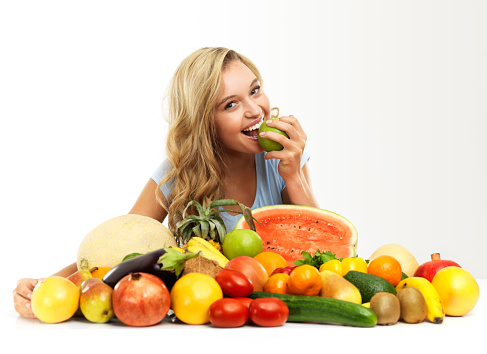 A pretty young woman biting into a delicious apple while surrounded by fresh produce