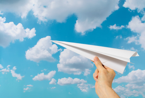 Close-up of holding a paper airplane, against blue sky with copy space.