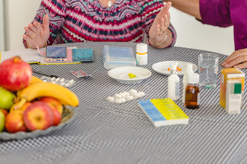 A devoted spouse supports her husband with dementia, ensuring he takes his prescribed medication at the kitchen table.