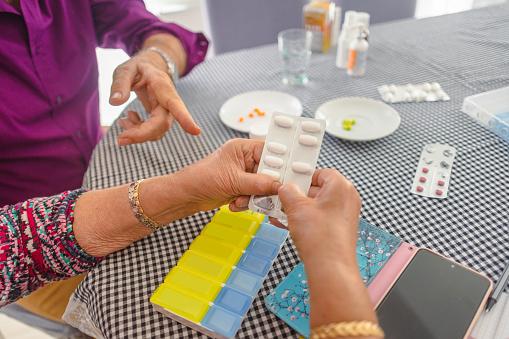 At the kitchen table, a wife assists her husband in managing his health by overseeing his dementia medication intake.