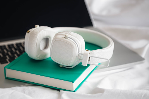 White headphones, book and laptop in a white bed, hobby, work at home, lazy day off.