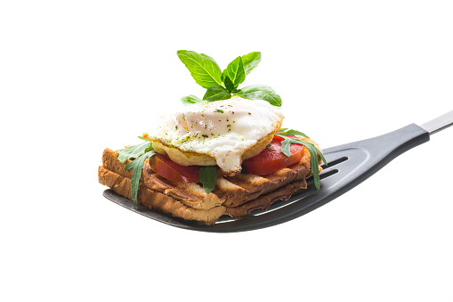 Prepared toast sandwich with fried egg with spices and herbs on a kitchen spatula.