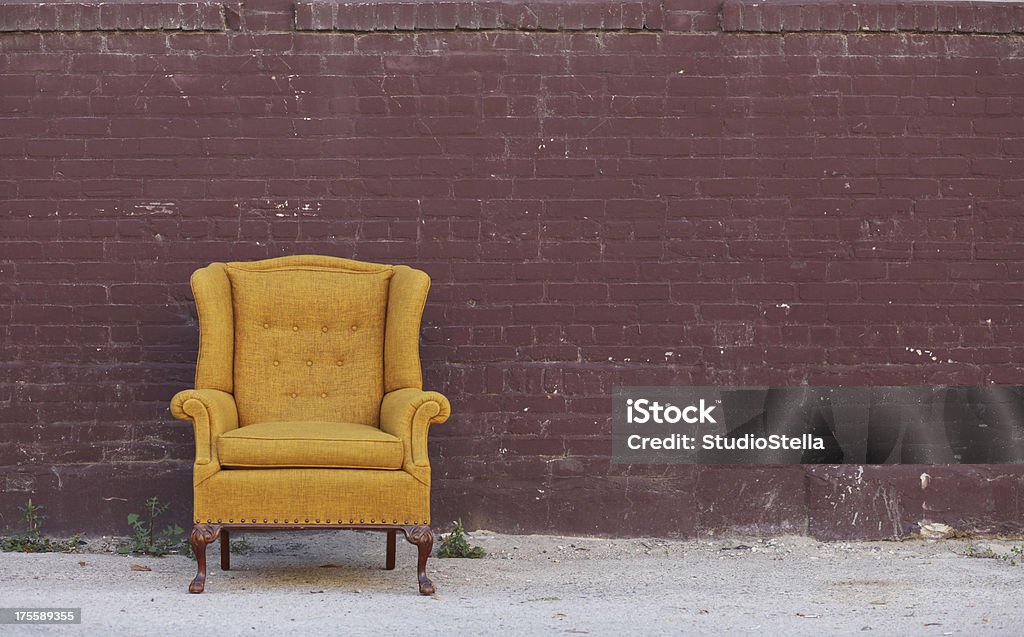 Vintage Wingback Chair & Brick wall Vintage gold wool upholstered wingback chair against a brick wall in an alley. Copyspace. Chair Stock Photo