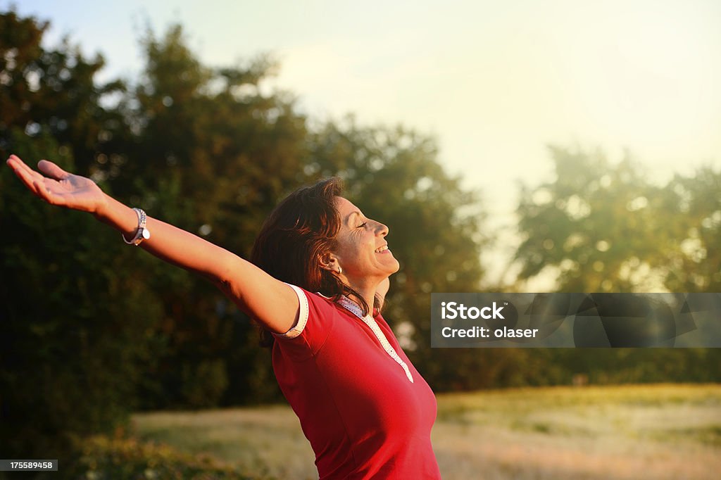 Happy woman on field "Smiling middle aged woman, arms / hands open, enoying the mild wind" 40-44 Years Stock Photo