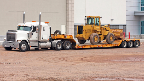 Side view of a parked semi truck equipped with a drop bed trailer ready to transport a pay loader.