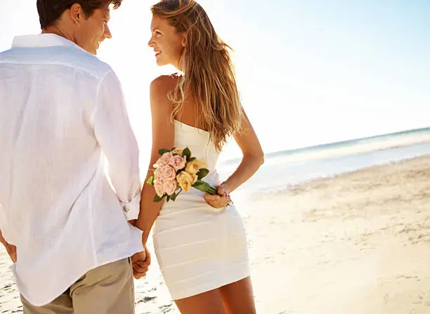 Rear view of a young man on the beach with his girlfriend holding flowers