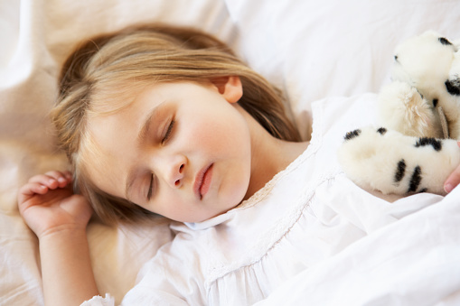 Young Girl Sleeping In Bed With Soft Toy
