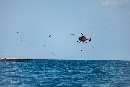 A helicopter is seen hovering over the ocean, preparing to land on a destination below