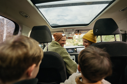 Photo of a smiling, cheerful family sitting in their car, all packed up and ready for an autumn adventure