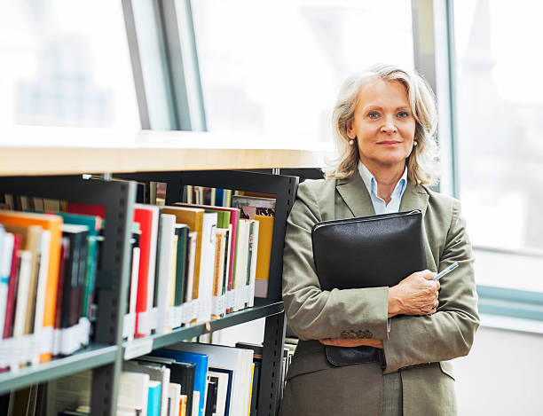 ältere frau stehend neben den bücherregalen. - professor librarian university library stock-fotos und bilder