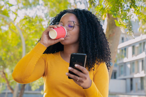 istock Young smiling black woman at mobile phone while drinking coffee. 1755948307
