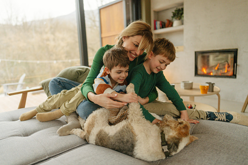 Photo of two young boys and their mommy, alongside with a family pet, cuddling and tickling on the couch in their living room