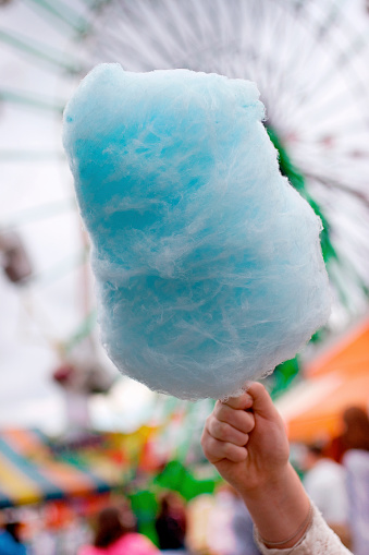 Child\'s hand holding up a cotton candy treat at a carnival.  Shallow dof.