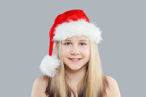Christmas child girl in red Santa hat on gray background