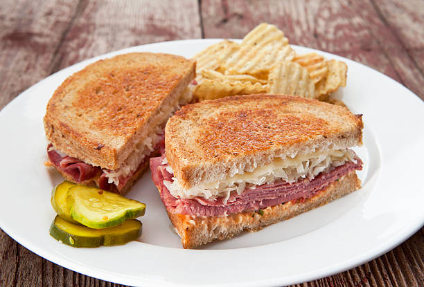 Reuben Sandwich Reuben sandwich with chips and pickles on a rustic wood table. reuben sandwich stock pictures, royalty-free photos & images