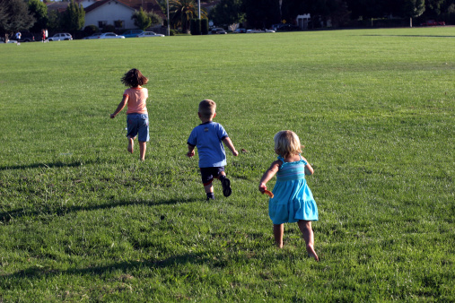 One boy and two girls running across green lawn