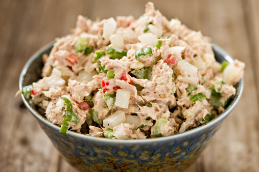 A high angle close up shot of a blue ceramic bowl full of freshly made tuna salad. Shot on an old wooden background.