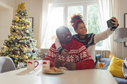 Father and daughter drinking tea and eating cookies. They are wearing Christmas sweaters and having good time together.