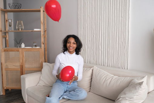 African american girl playing on sofa with red heart shape balloons. valentines day.