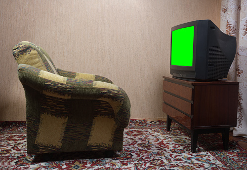 Old black TV with green screen and chair from the 1980s and 1990s.