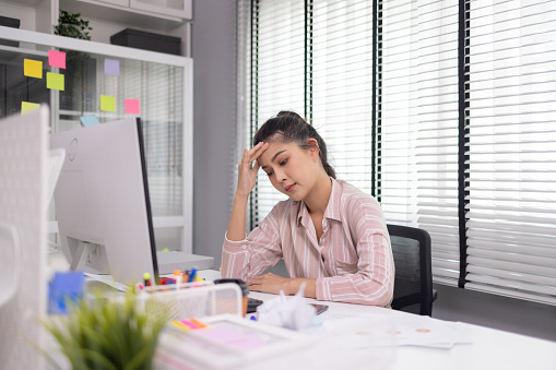 Asian woman is stressed while working in the office, Tired Asian businesswoman with headache and migraine at the office, feeling sick at work.