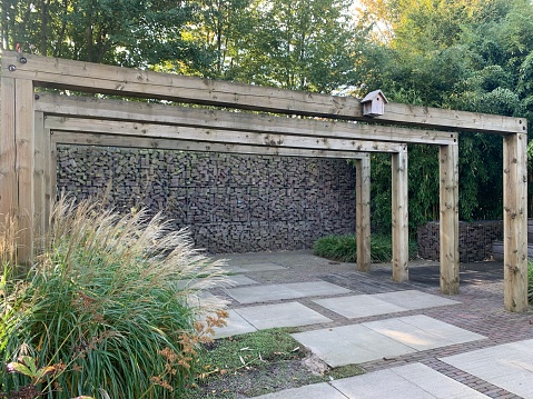 Pergola made of wooden beams. Paving the yard with large tiles goes well with the durability of gabions. Plant: Miscanthus chinensis